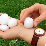 A man holding a handful of large, golf-ball sized pieces of hailstones.