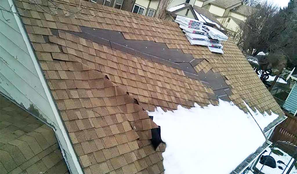 Damaged roof with sections of shingles crumpled and sliding off.